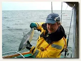 Angler in Regenkleidung hält an Bord eines Bootes einen Lachs hoch