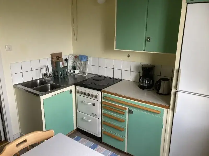 Kitchen with green cupboard doors, cooker, sink and coffee maker