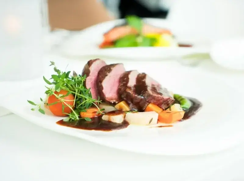 Sliced meat with root vegetables and sauce on a white plate