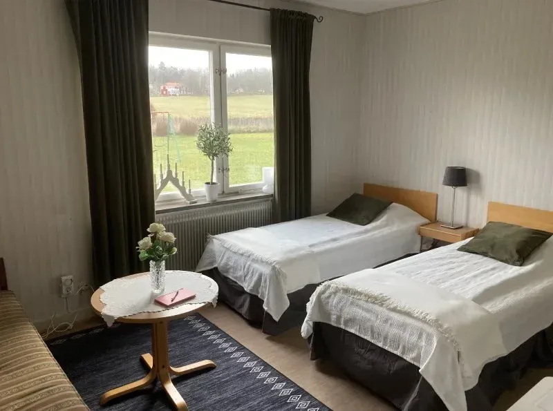 Room with two single beds, a sofa and a small table by the window