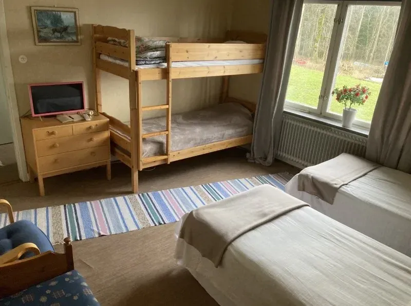 Room with a bunk bed, two single beds, a chest of drawers and a TV